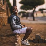 Happy boy sitting on a dusty sidewalk in Pretoria, South Africa, smiling warmly.