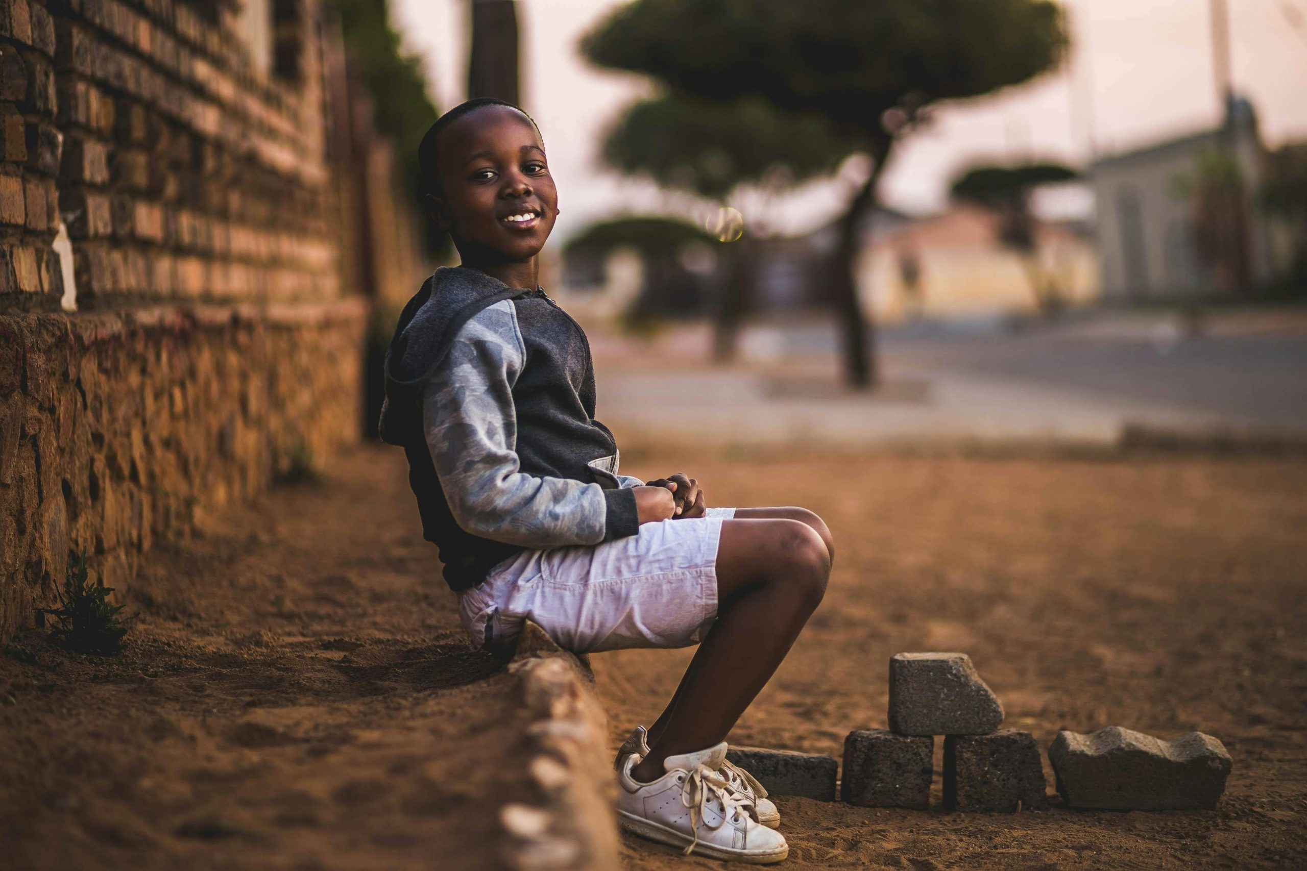 Happy boy sitting on a dusty sidewalk in Pretoria, South Africa, smiling warmly.