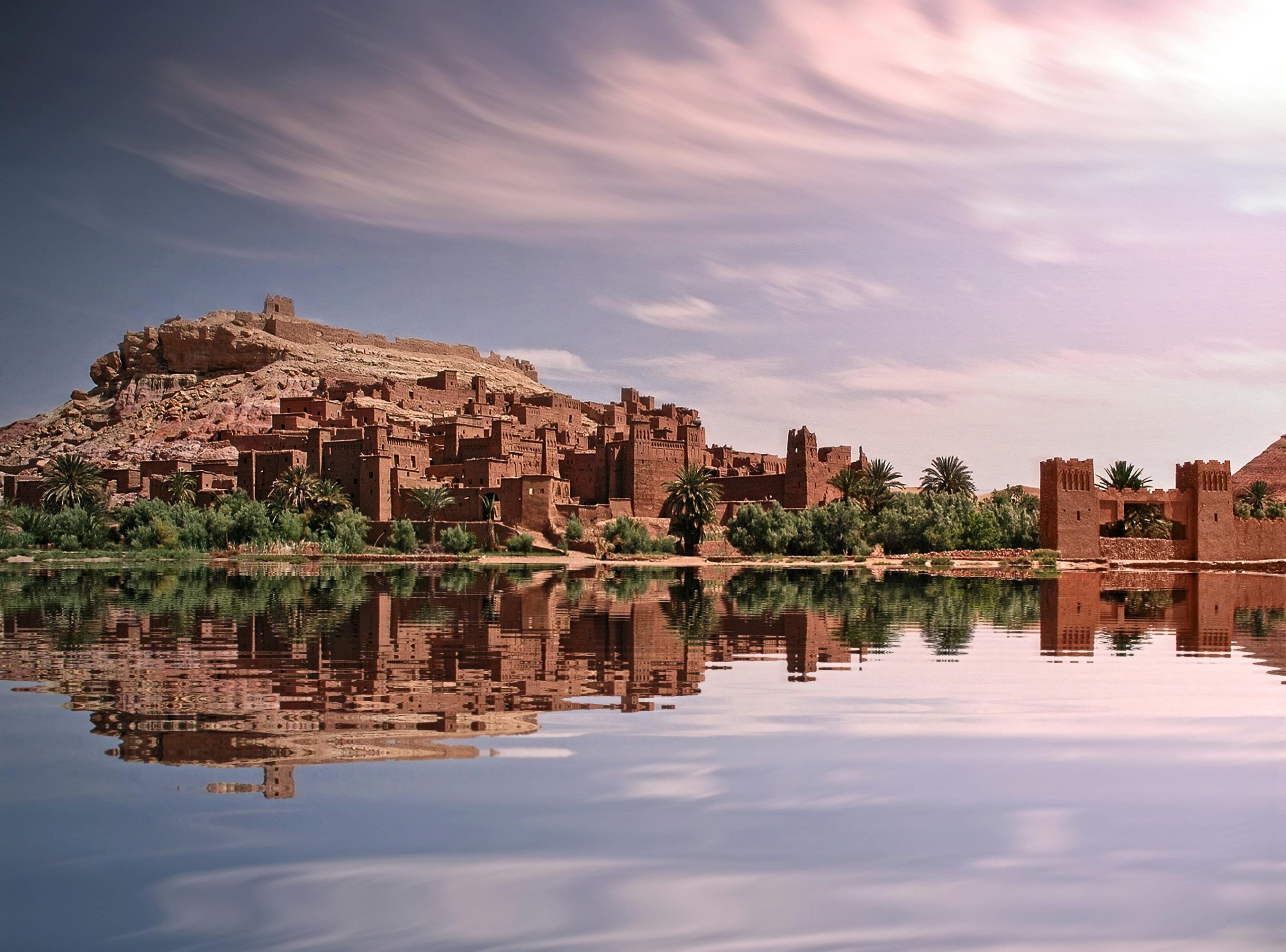 Picturesque reflection of Ouarzazate's historic ksar by the river under a vibrant sky.